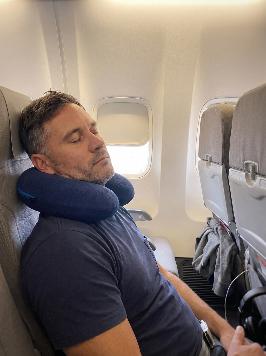 Traveler asleep in a window seat with the navy travel pillow